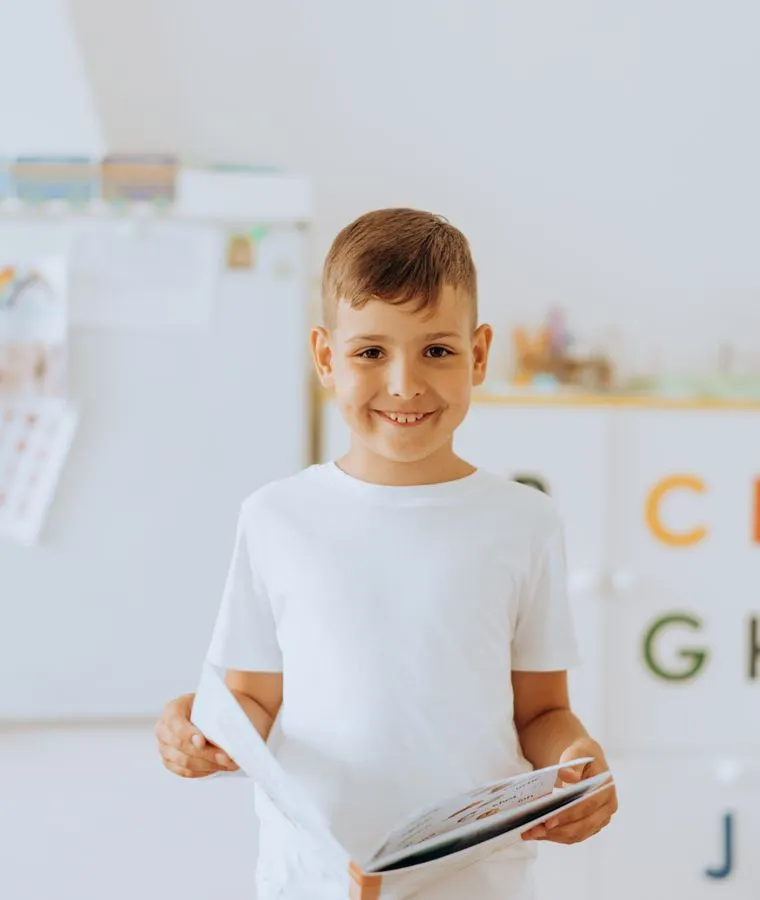 A cheerful child holding a book in a classroom
